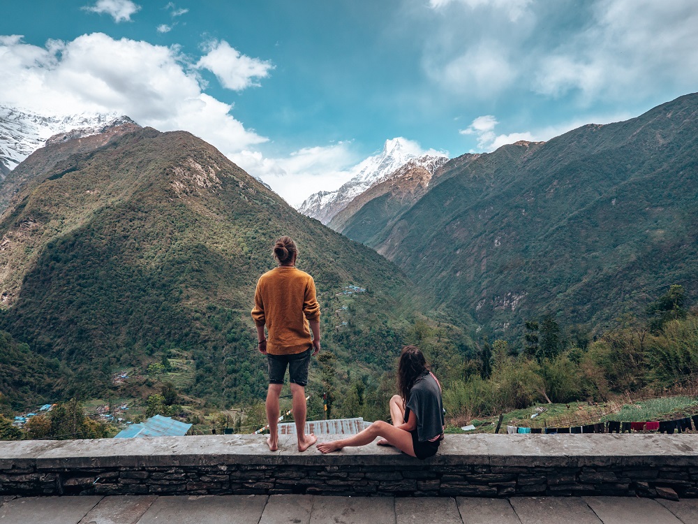 nepal trekking - Ein Mann und eine Frau sitzen auf einer Mauer und blicken auf die Berge in Nepal