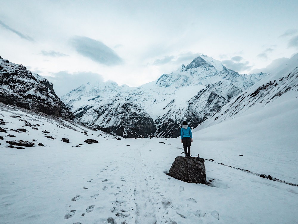 nepal trekking - Person standing on a stone, surrounded by snow and looking at the mountains in the distance