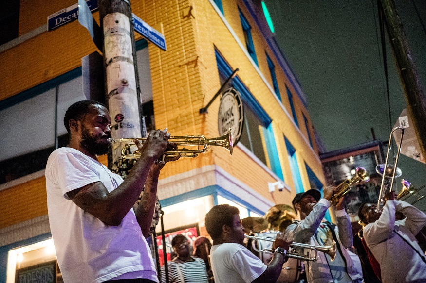 where to stay in new orleans, a group of musicians playing trumpets on the corner of a street at night