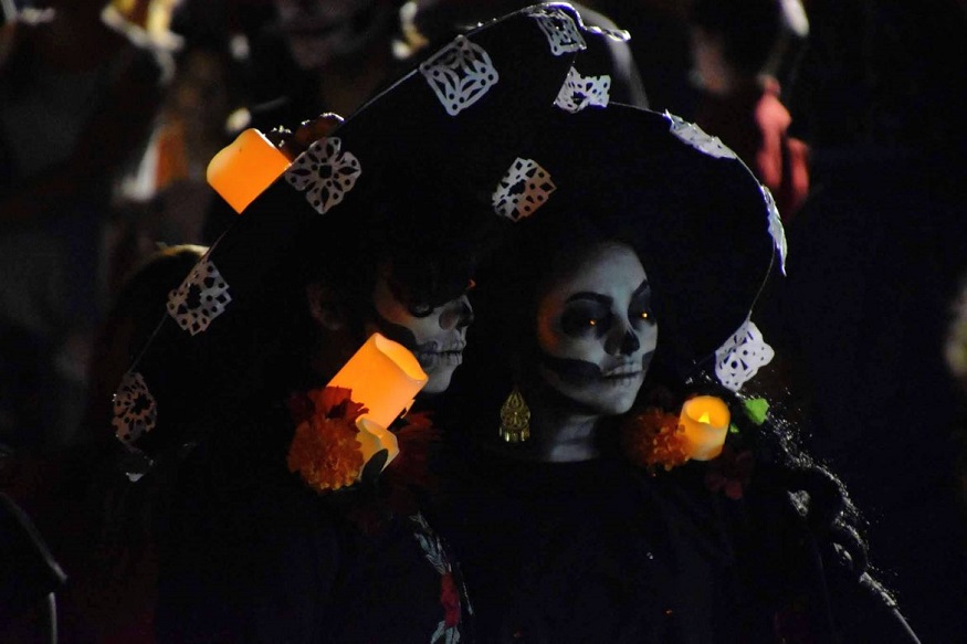 day of the dead facts, two people dressed in black celebrating day of the dead with candles and skeleton faces
