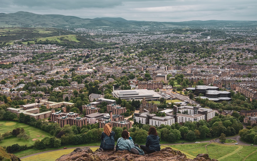 edinburgh on a budget, 3 people sitting on top of Arthur's seat overlooking the city