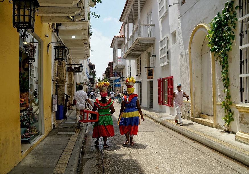 best places to visit in colombia, two women in traditional dress walking down the street in Cartagena