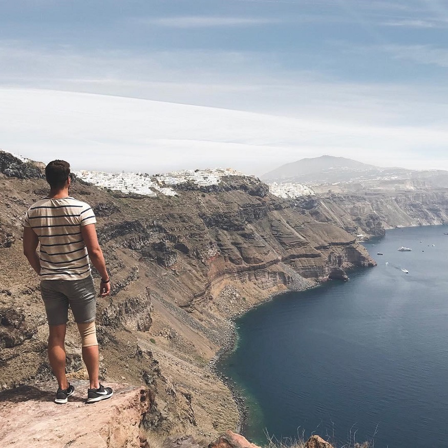 best romantic destinations for solo travellers, man standing on cliffs by the sea in santorini