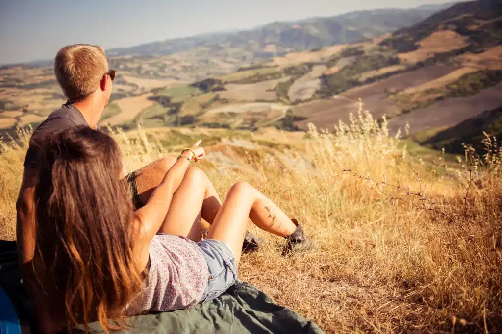 two people sitting in a field, the woman pointing at the view, while they both look that way