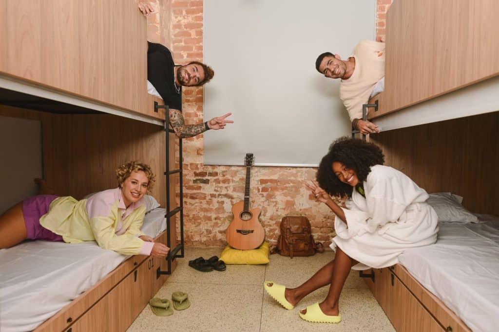 a hostel dorm with two women and two men smiling at the camera in their bunk beds