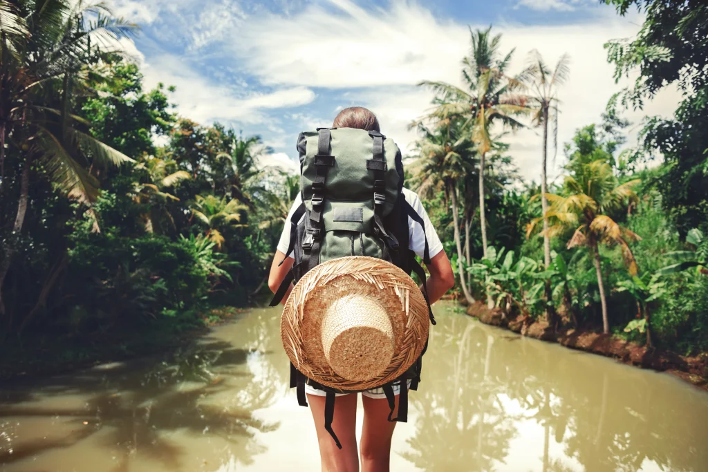 Traveler woman with backpack standing near big tropical river at sunny day 