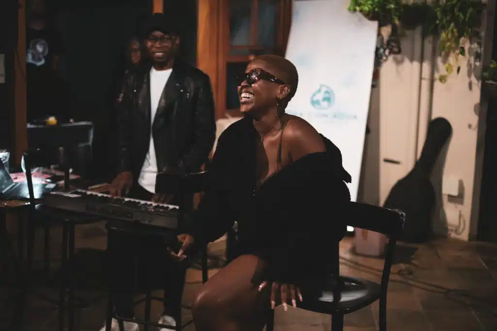 woman laughing, sitting on a stool, after singing live with man on keyboard next to her