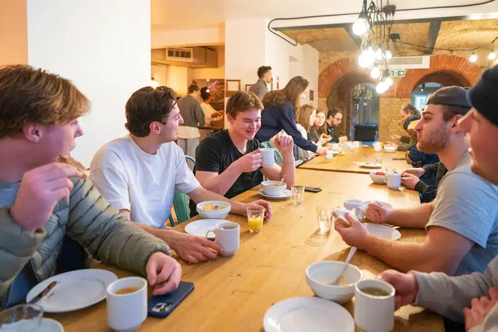 group of men sitting at a table at a hostel talking and eating a meal together