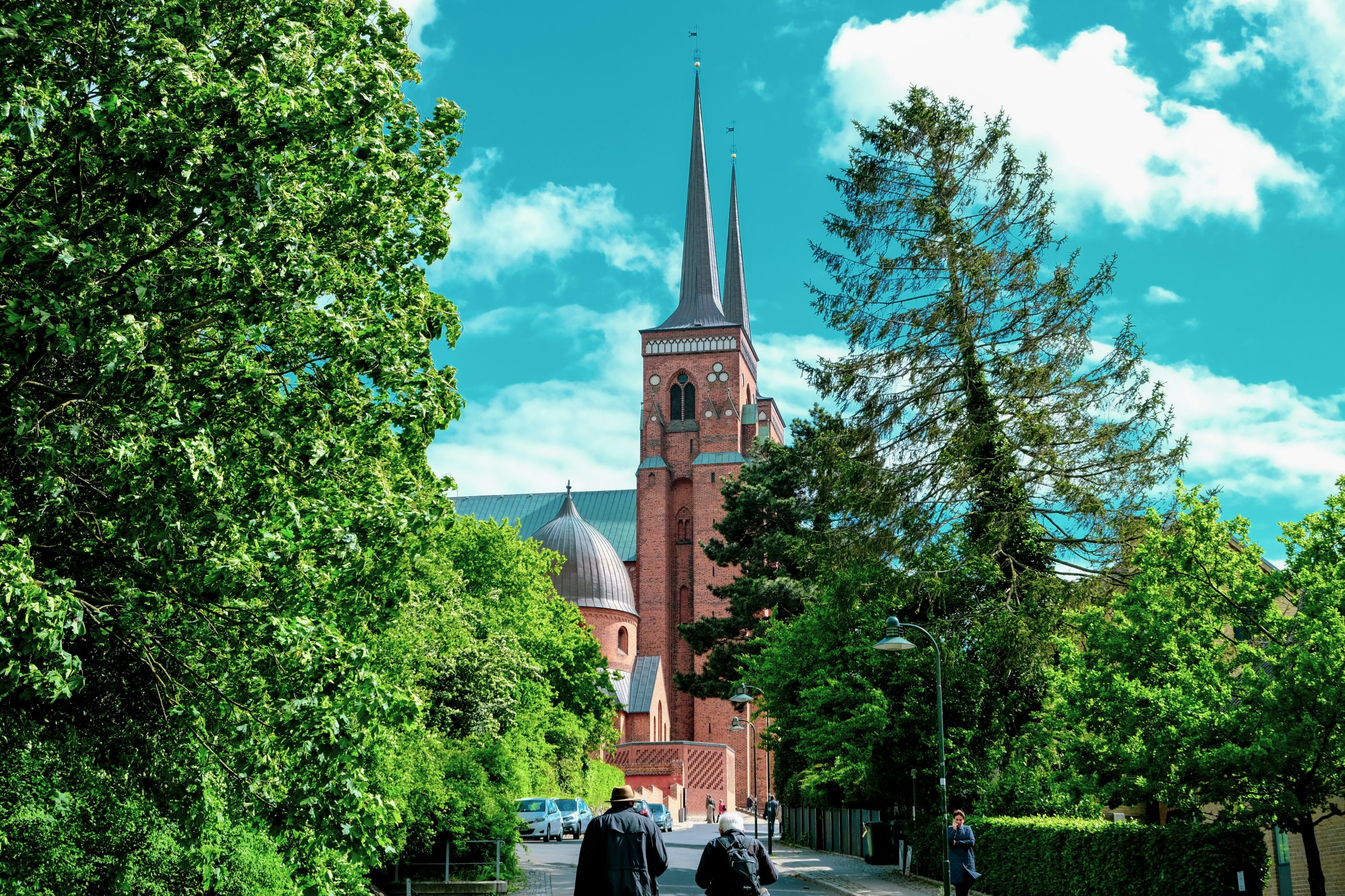 two people walking down a street in front of a church in Roskilde, denmark. day trips from copenhagen