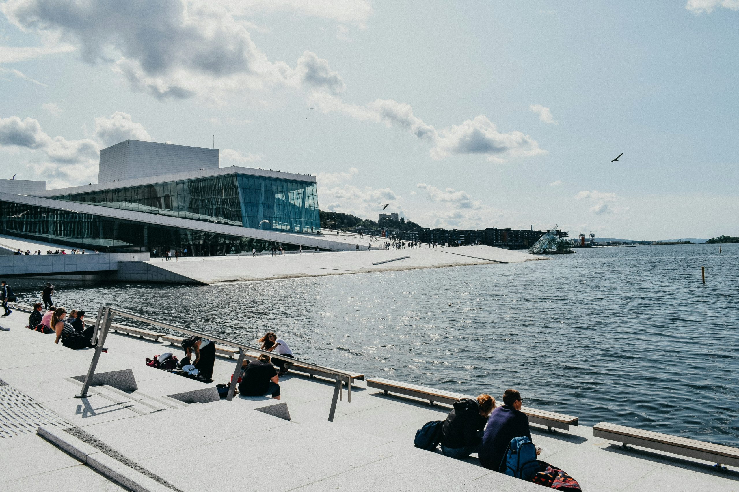 people sitting beside the water by the oslo opera