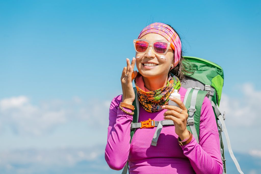 Hiker woman applying sun cream to protect her skin from dangerous uv sun rays high in mountains. Travel healthcare concept 
