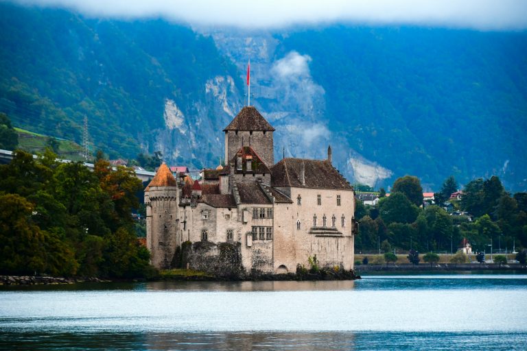 a castle sitting on top of a lake surrounded by mountains, day trips from geneva
