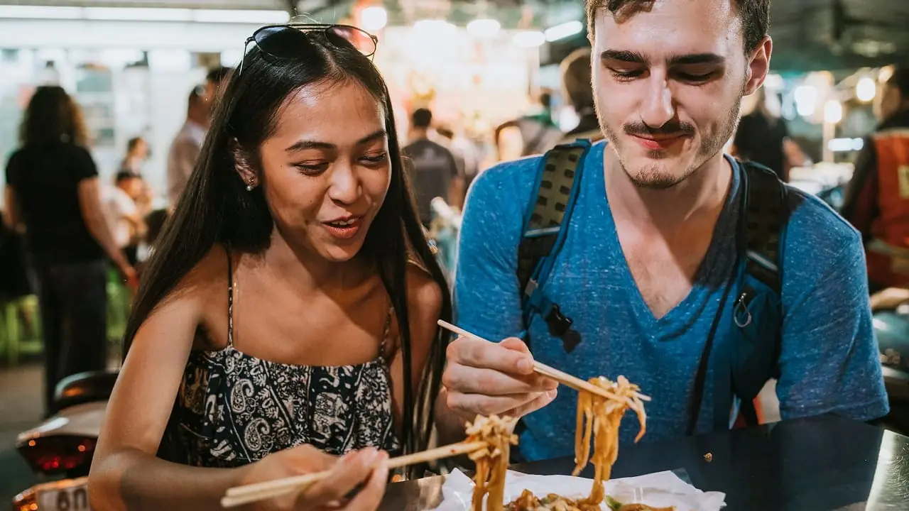 Two travellers eating noodles at a night market