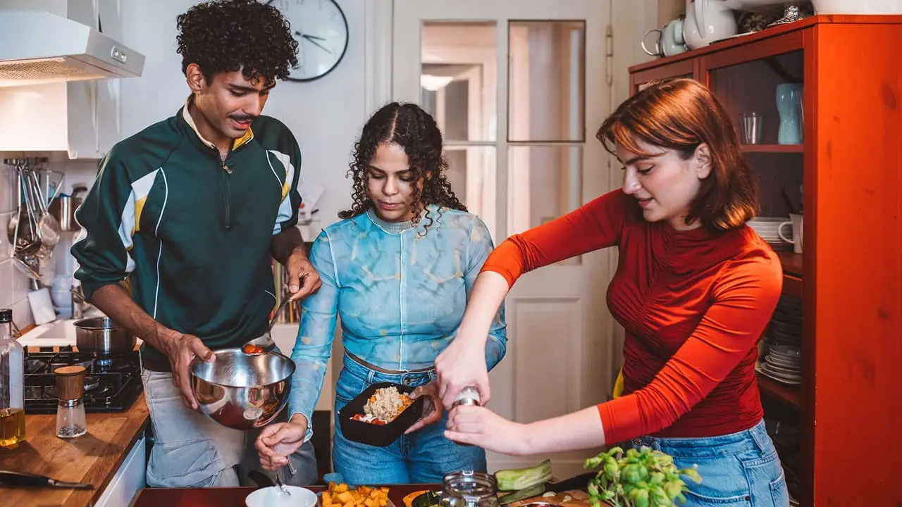 Three travellers cooking together in a hostel kitchen